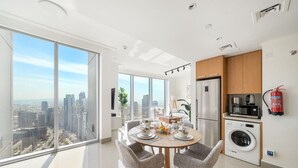 A modern apartment with a dining area, kitchen, and a large window offering a city view.