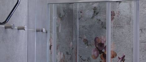 A shower with a glass enclosure and floral-patterned tiles.
