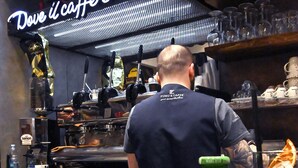 A barista preparing a drink behind a counter with a neon sign above. - Incoming Roof Bovio (Naples)