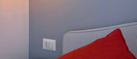 A neatly made bed with a red pillow, a bedside table, and a hanging light fixture.