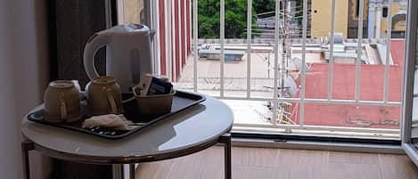 Een balkon met een tafel waarop een waterkoker, bekers en een dienblad staan, met uitzicht op een haven met gebouwen en een gebouw met een rood dak.
