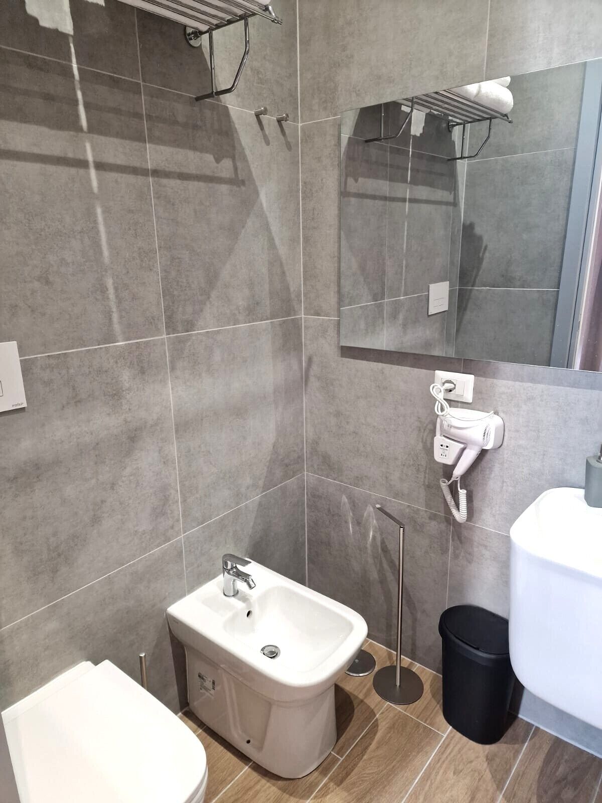 A modern bathroom with a bidet, a toilet, a sink, a mirror, and a hairdryer mounted on the wall.
