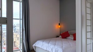 A bedroom with a bed, a window with curtains, a hanging light, and a view of buildings outside. - Incoming Roof Bovio (Naples)
