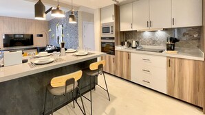 A modern kitchen with a central island, bar stools, a microwave, oven, and a sink. - C Living - Premium 3 Bedroom - AQIQ (Riyadh)