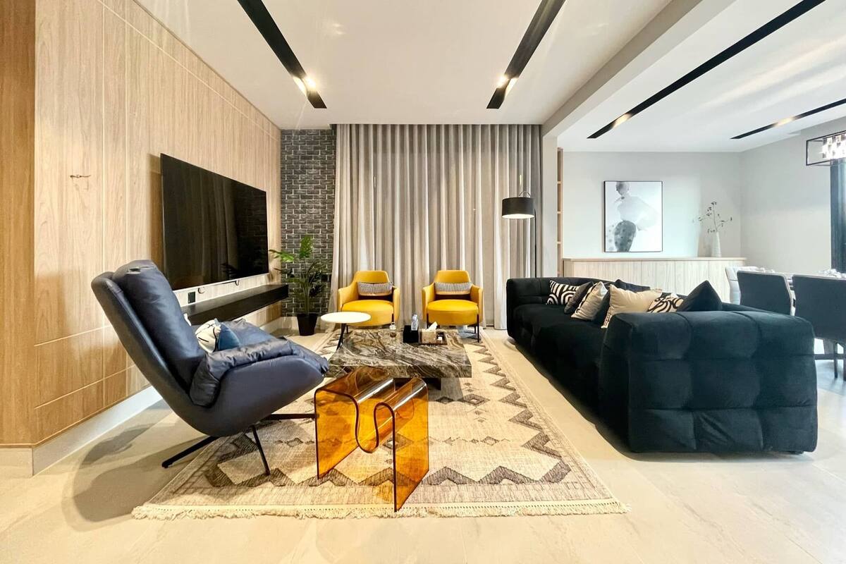 A modern living room with a sofa, two armchairs, a coffee table, and a TV mounted on the wall.