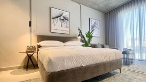 A modern bedroom with a large bed, a bedside table, a lamp, and two abstract art pieces on the wall. - C Living - Premium 3 Bedroom - AQIQ (Riyadh)