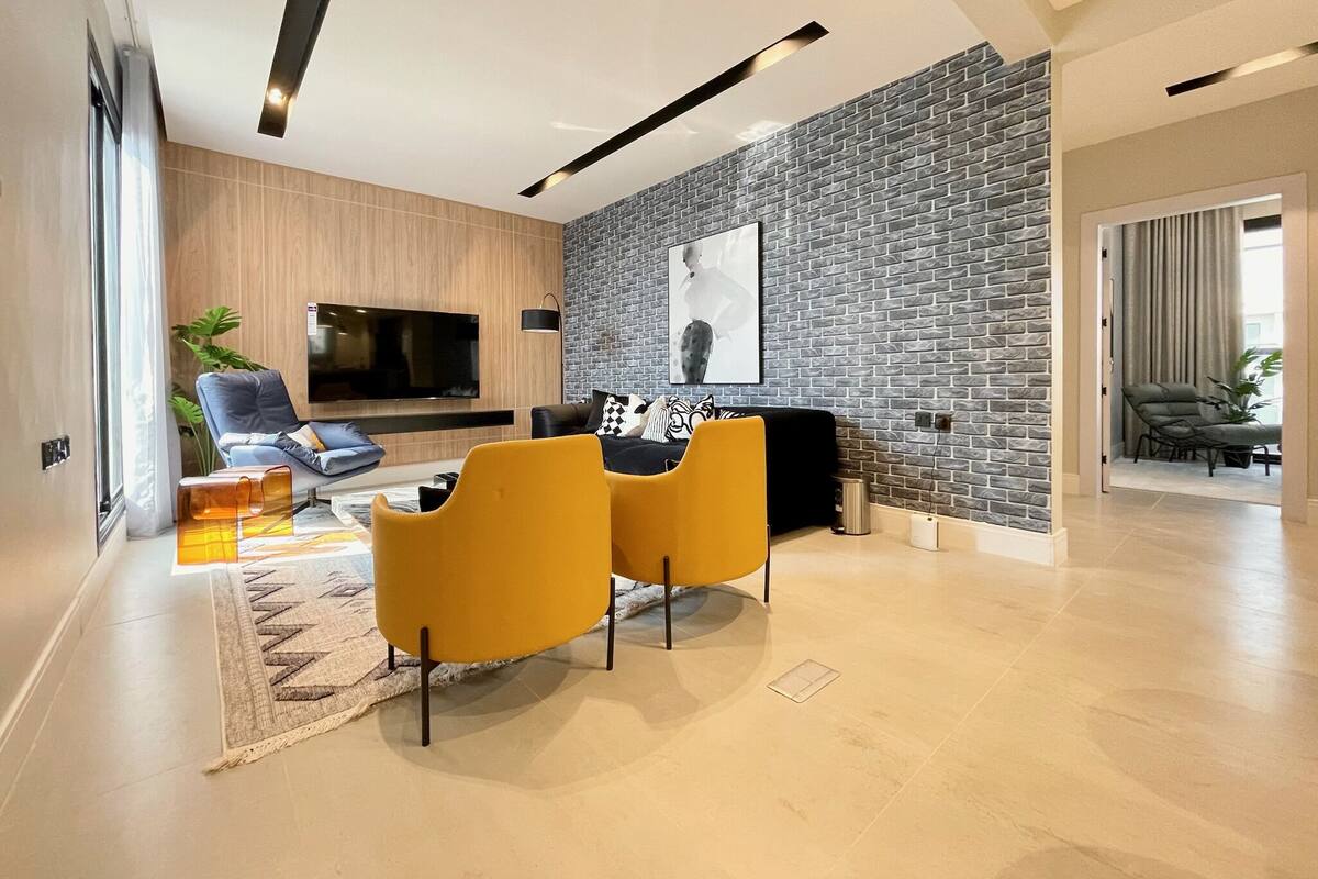 A modern living room with a flat-screen TV, a sofa, and two yellow chairs.