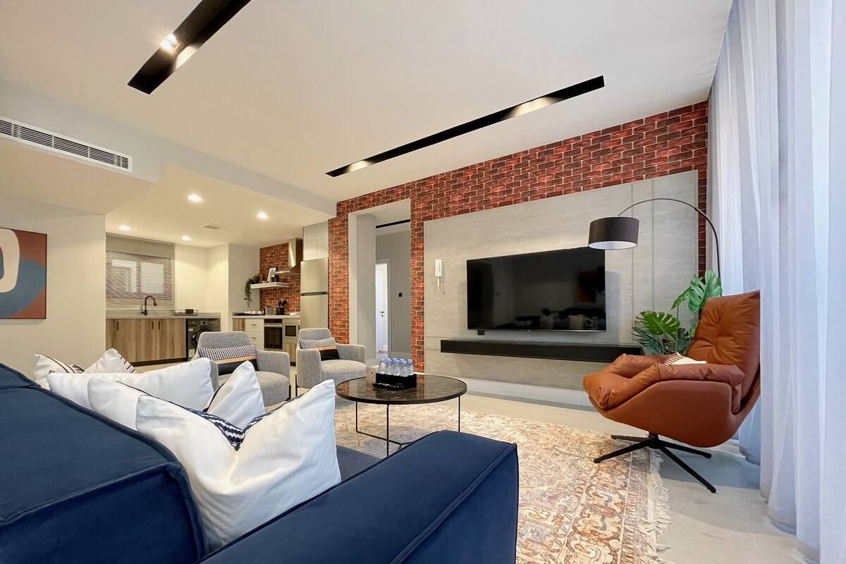 A modern living room with a sofa set, a coffee table, and a TV mounted on a brick wall.