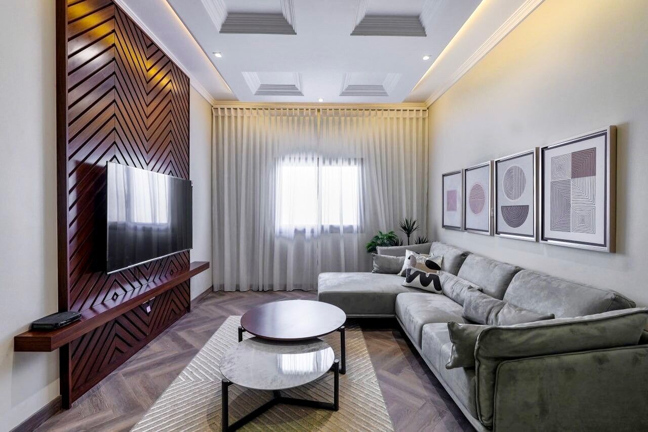 Un salon moderne avec un téléviseur à écran plat, un canapé gris, une table basse ronde et un mur d’accent en bois.