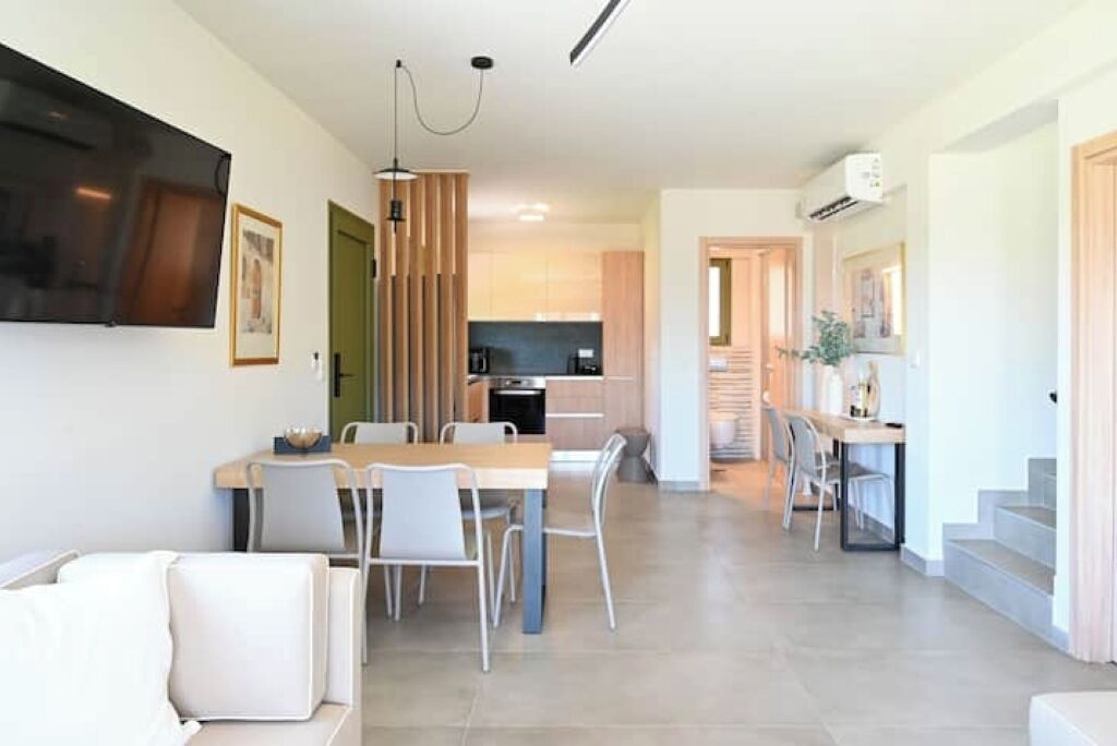 A modern kitchen with a dining area, a staircase, and a living room with a sofa.