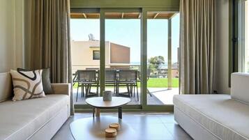 A modern living room with a sofa, a coffee table, and a view through a glass door to an outdoor area with a table and chairs.
