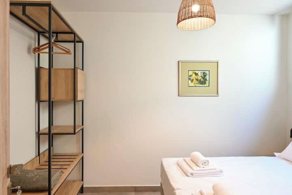 A bedroom with a bed, a hanging wooden shelf, a framed picture on the wall, and a pendant light.
