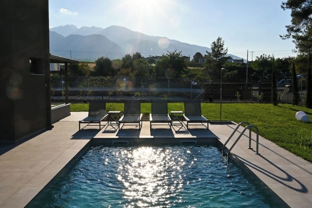 A swimming pool with sun reflecting on the water, surrounded by lounge chairs and a view of mountains in the background.