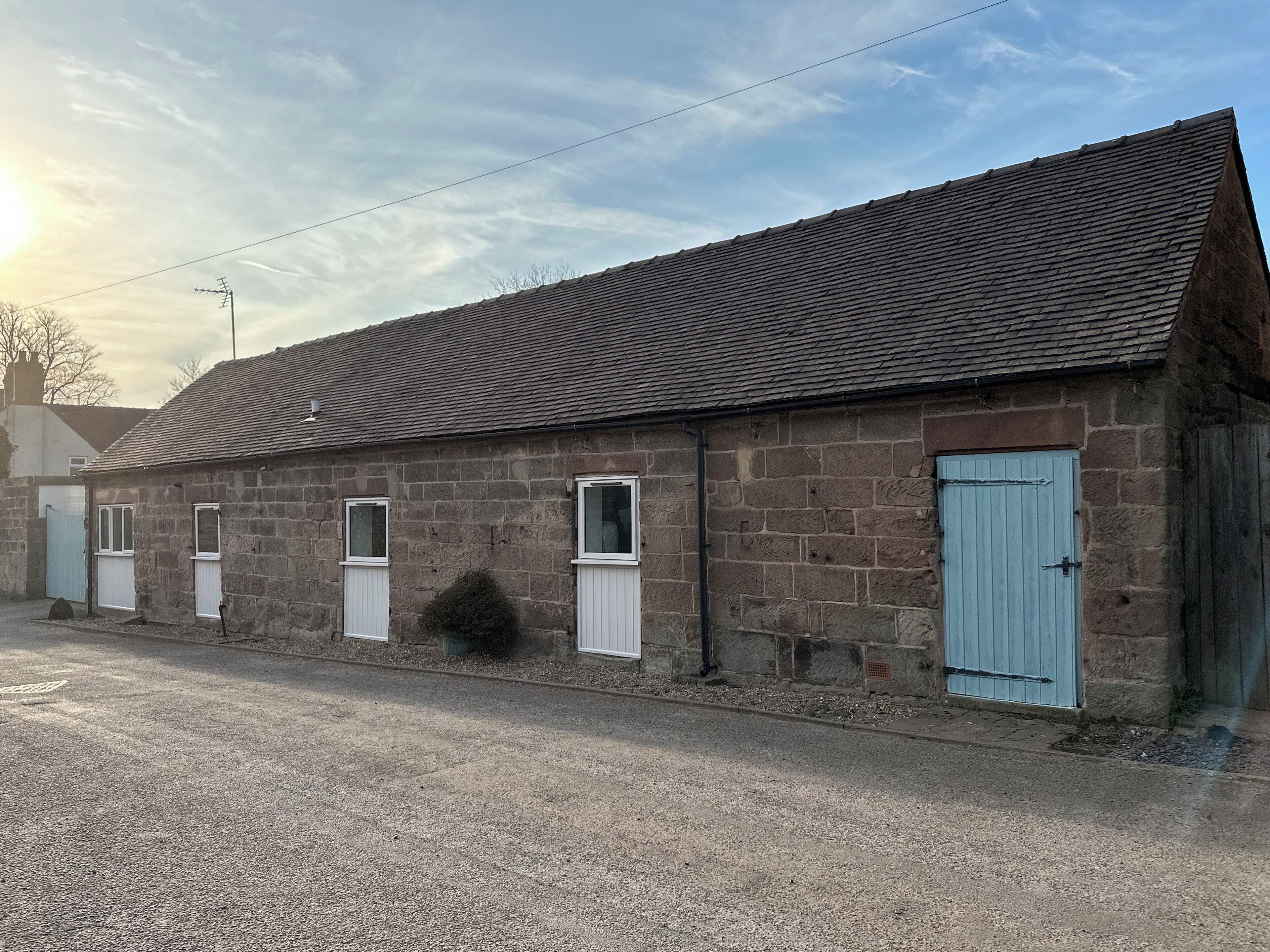A stone building with a sloped roof, multiple small windows, and a blue door.