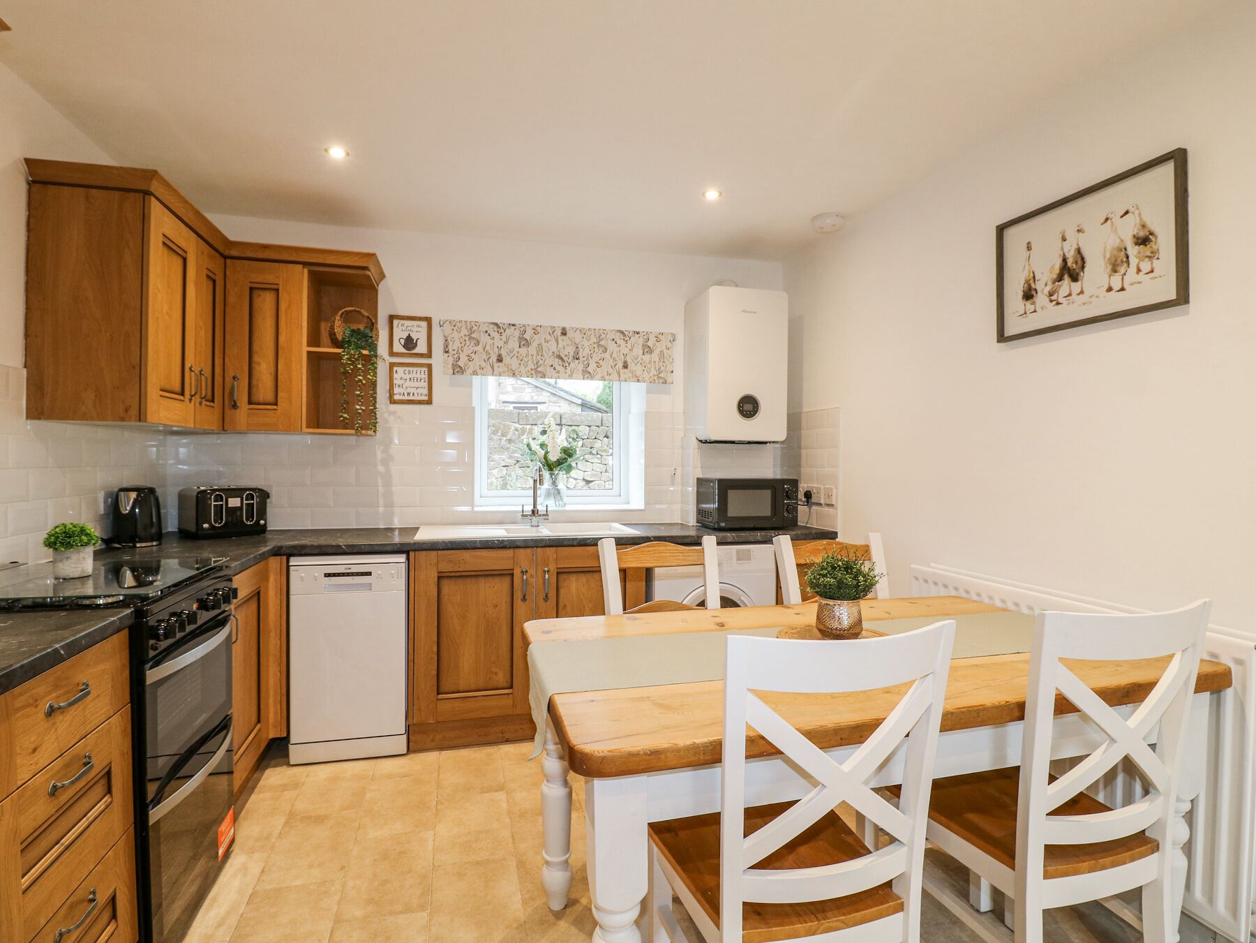 A modern kitchen with wooden cabinets, a dining table with chairs, a microwave, and a coffee machine.