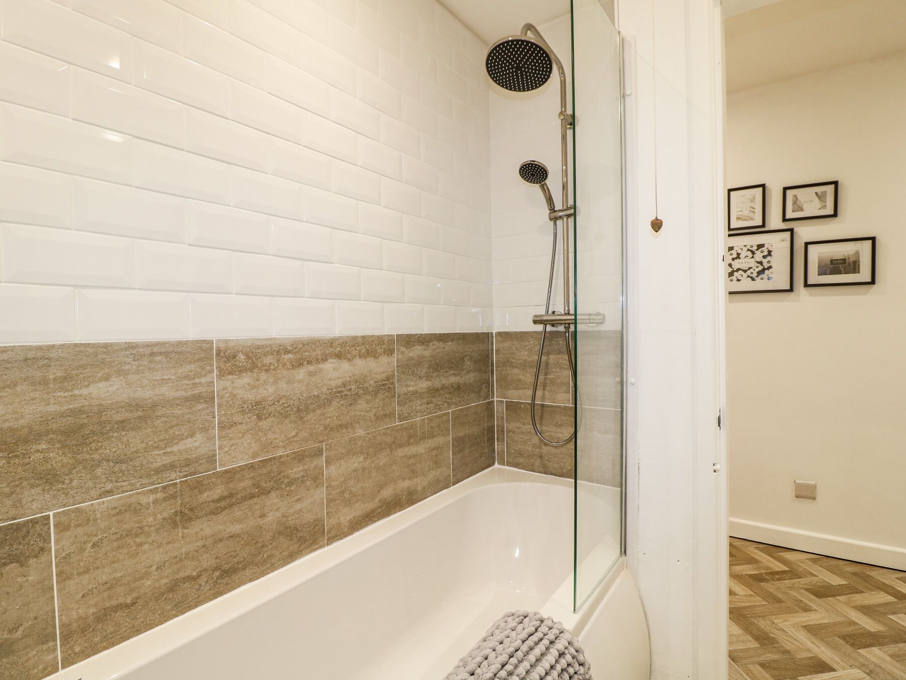 A modern bathroom with a glass-enclosed shower, white and brown tiles, and a wooden floor.