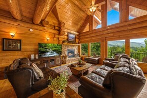 A log cabin interior with a stone fireplace, leather furniture, and a large TV. - Bella Vista Lodge: Where Beautiful Begins (Gatlinburg)