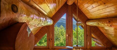 A wooden cabin with a sloped roof, a ceiling fan, and a view of green trees through a window.