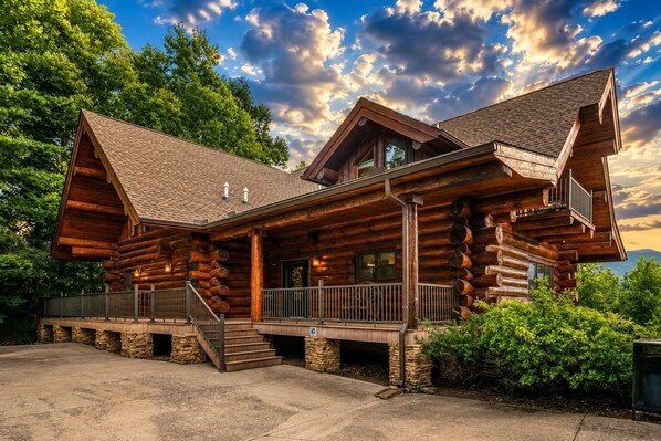 A log cabin with a porch, a staircase, and a view of the surrounding forest.