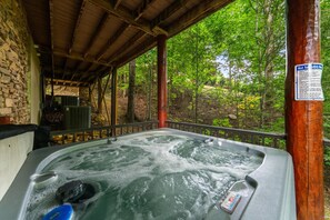 A hot tub under a wooden canopy with a stone wall and a view of a forest.