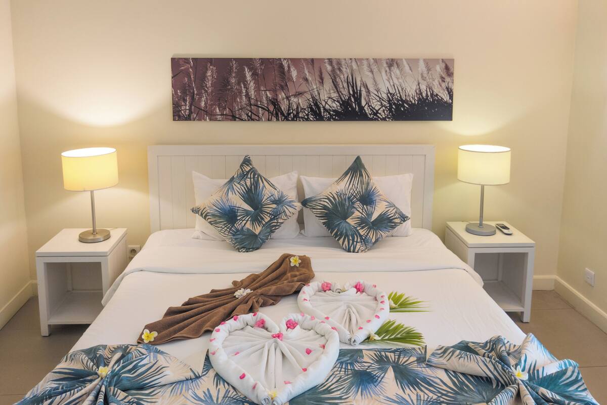 Una cama bien hecha con almohadas de temática tropical, una toalla y un lei decorativo.