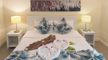 A neatly made bed with tropical-themed pillows, a towel, and a decorative lei.