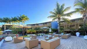 Eine Holzterrasse mit Korbmöbeln und Sonnenschirmen, umgeben von Palmen und einem Pool.