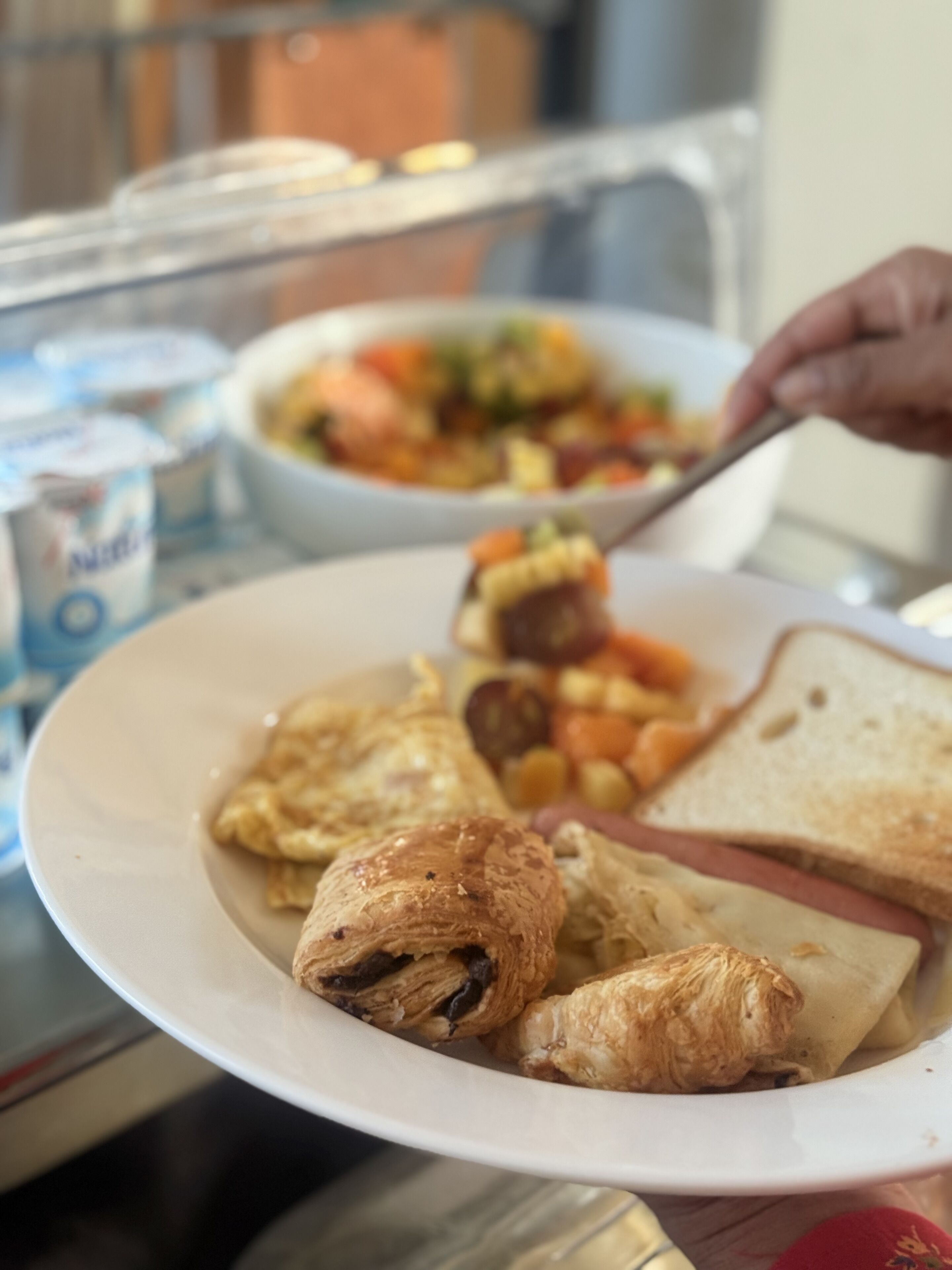 A plate with croissants, ham, and toast, and a bowl of salad in the background.