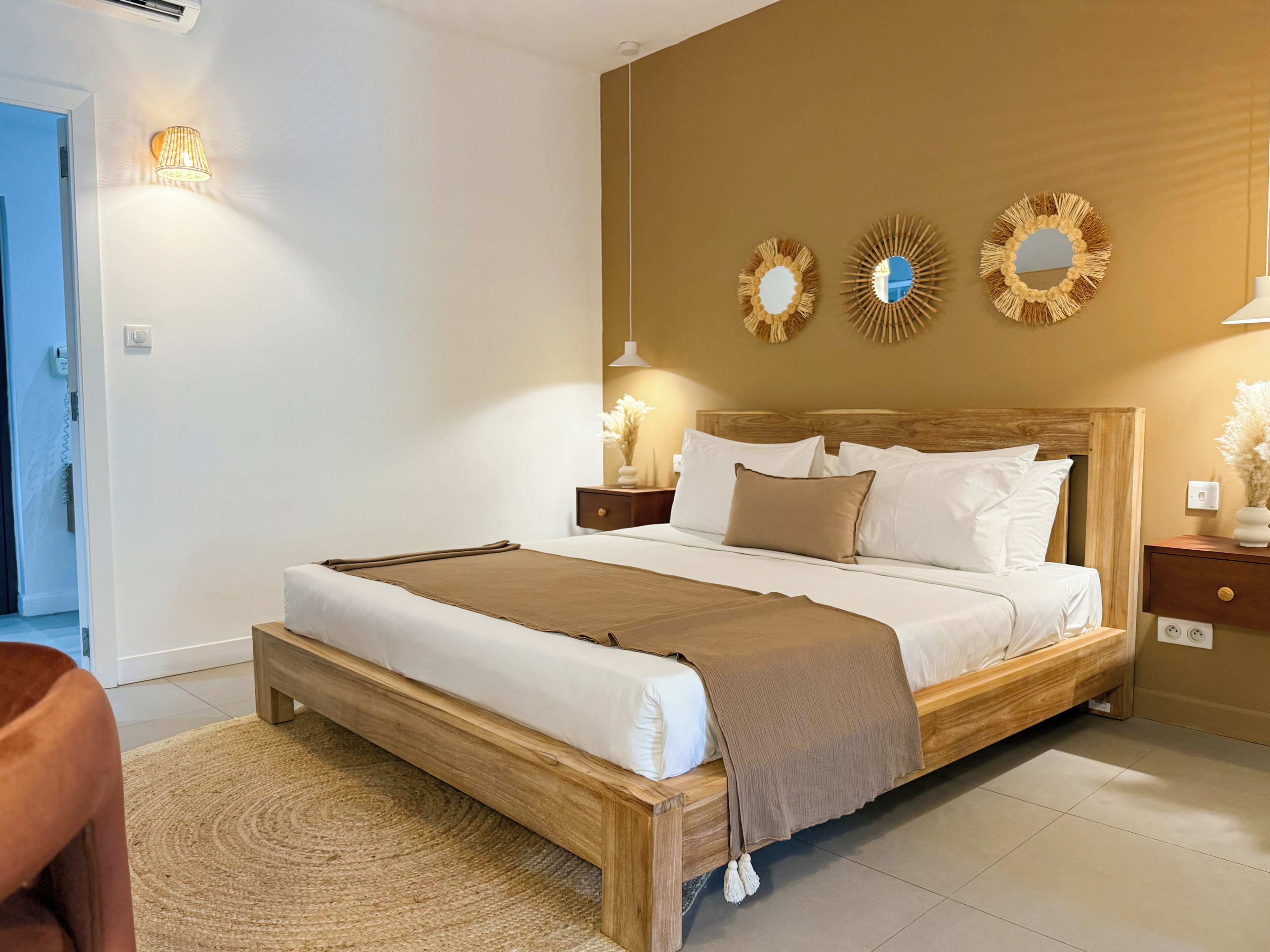 A bedroom with a wooden bed, white bedding, a brown throw blanket, and decorative wall mirrors.