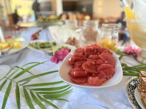 A buffet table with various food items, including a plate of sliced meat, a bowl of fruit, and some condiments.