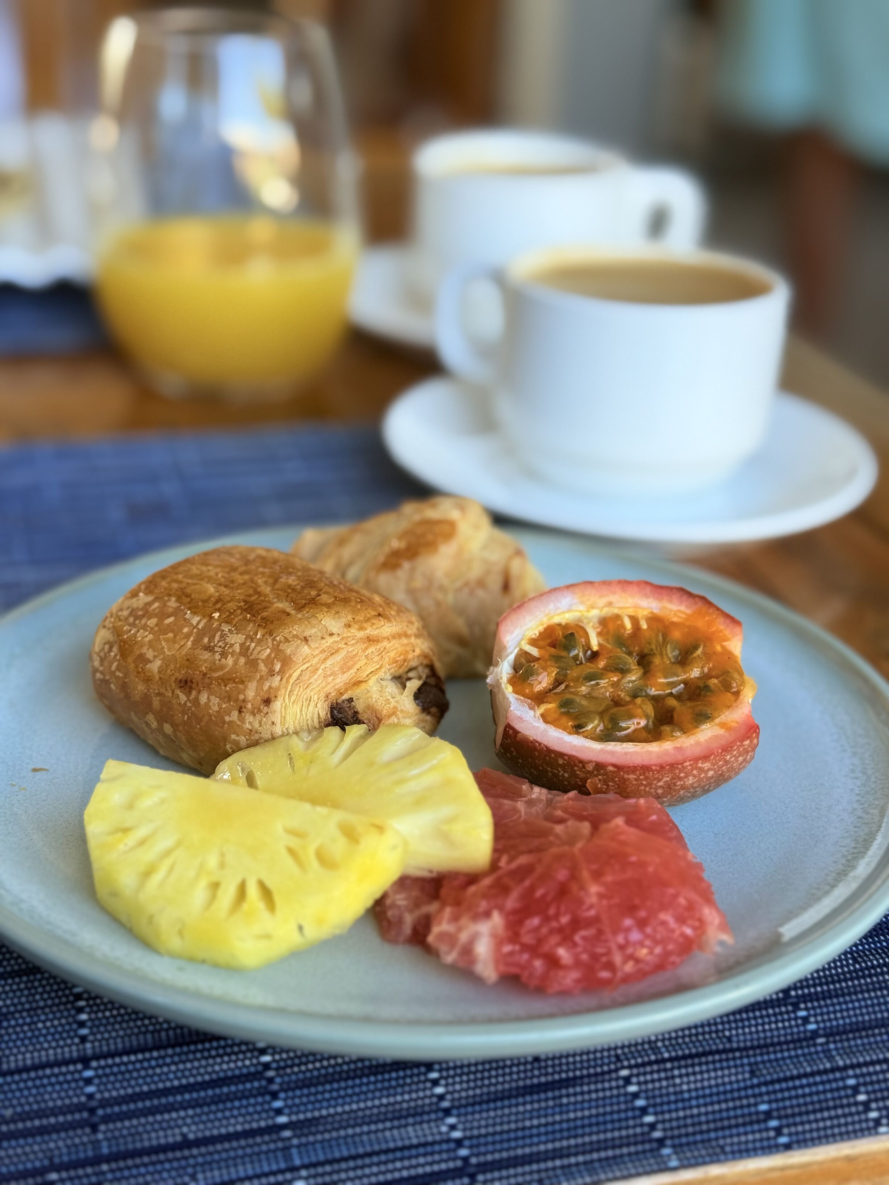 Un plato de desayuno con pasteles, fruta y un maracuyá cortado por la mitad sobre una base azul.