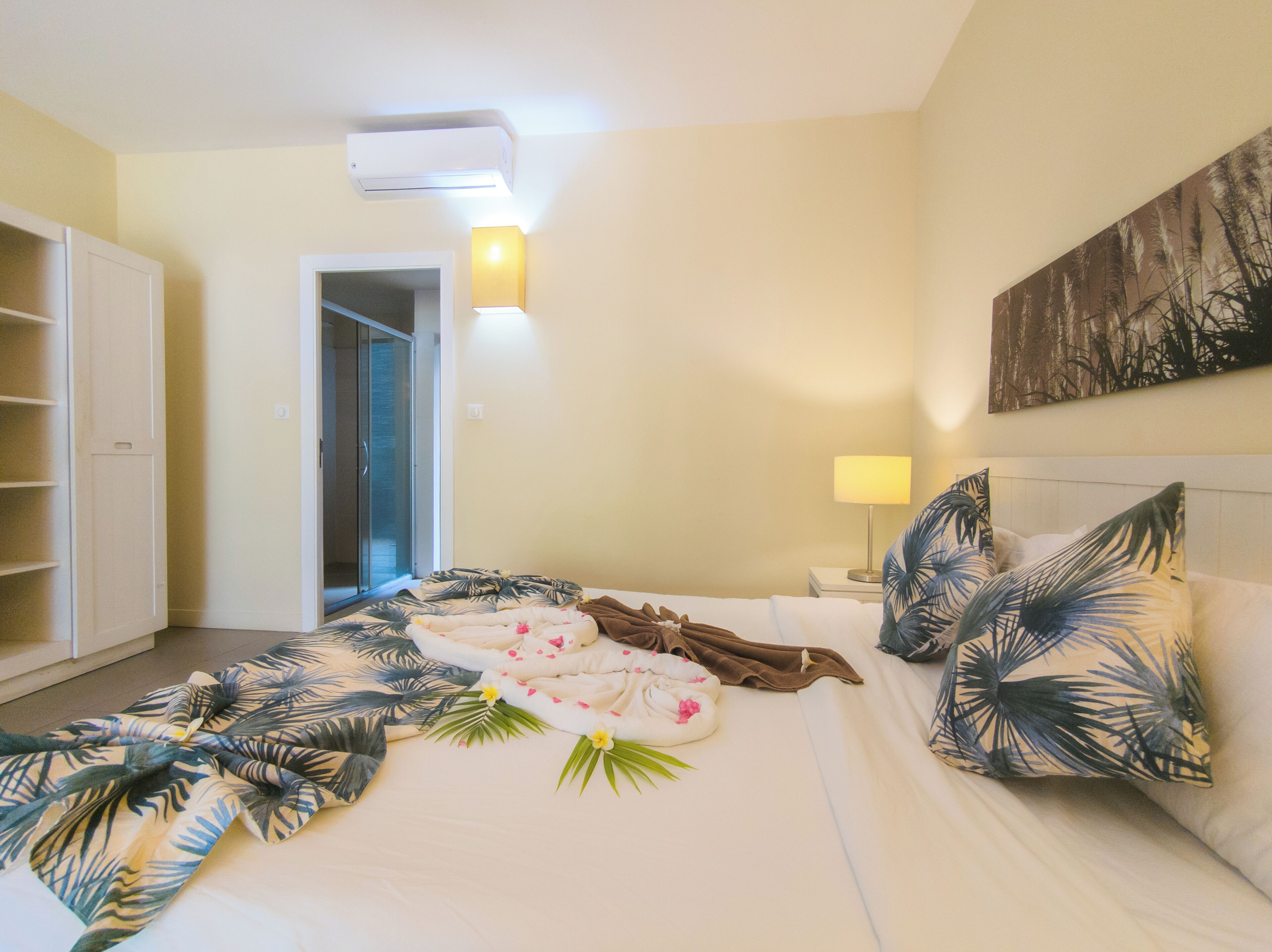 A hotel room with a bed, a nightstand, a lamp, a painting on the wall, and a wardrobe.