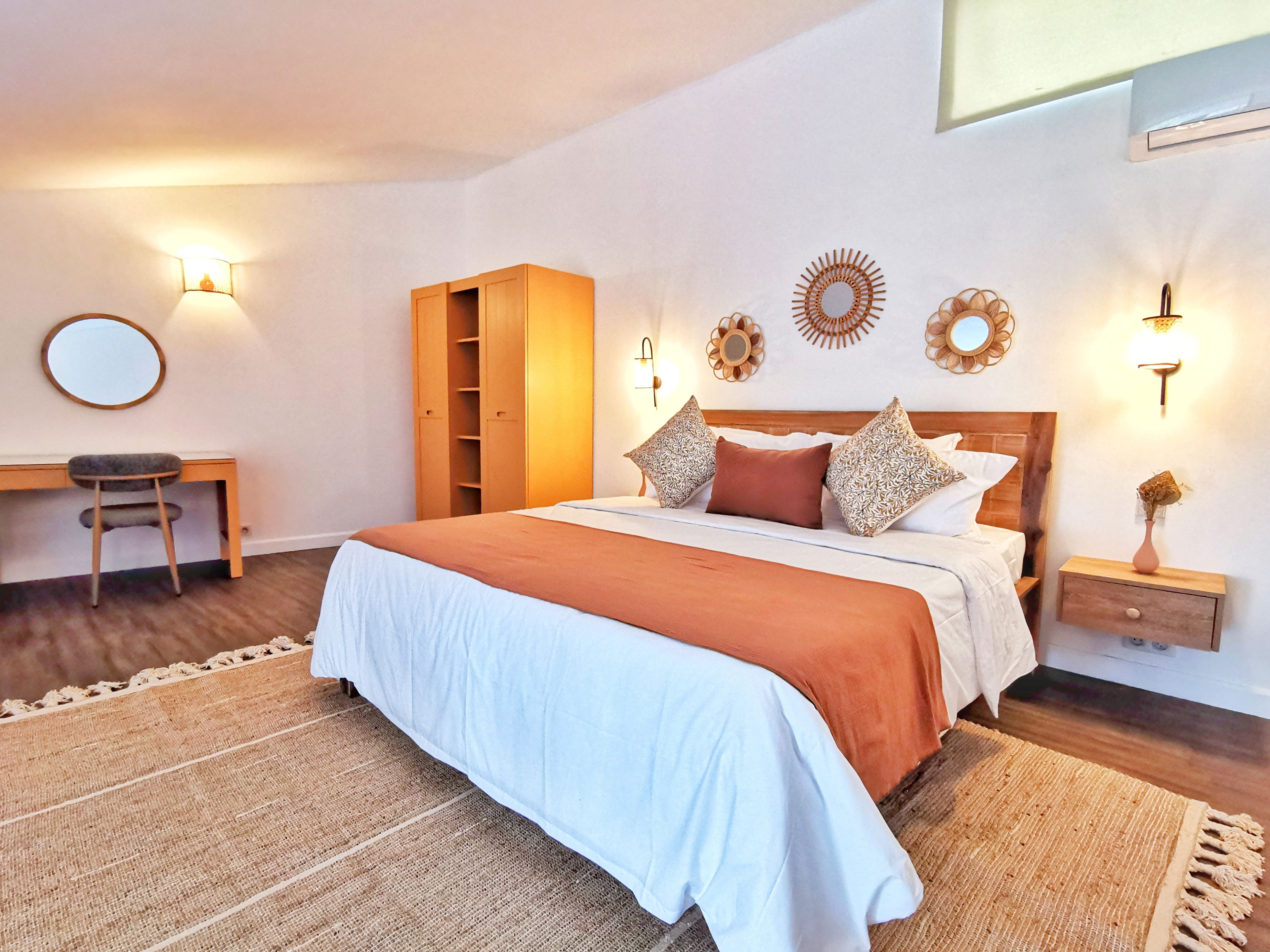 A bedroom with a bed, a desk, a wardrobe, and wall-mounted lights.