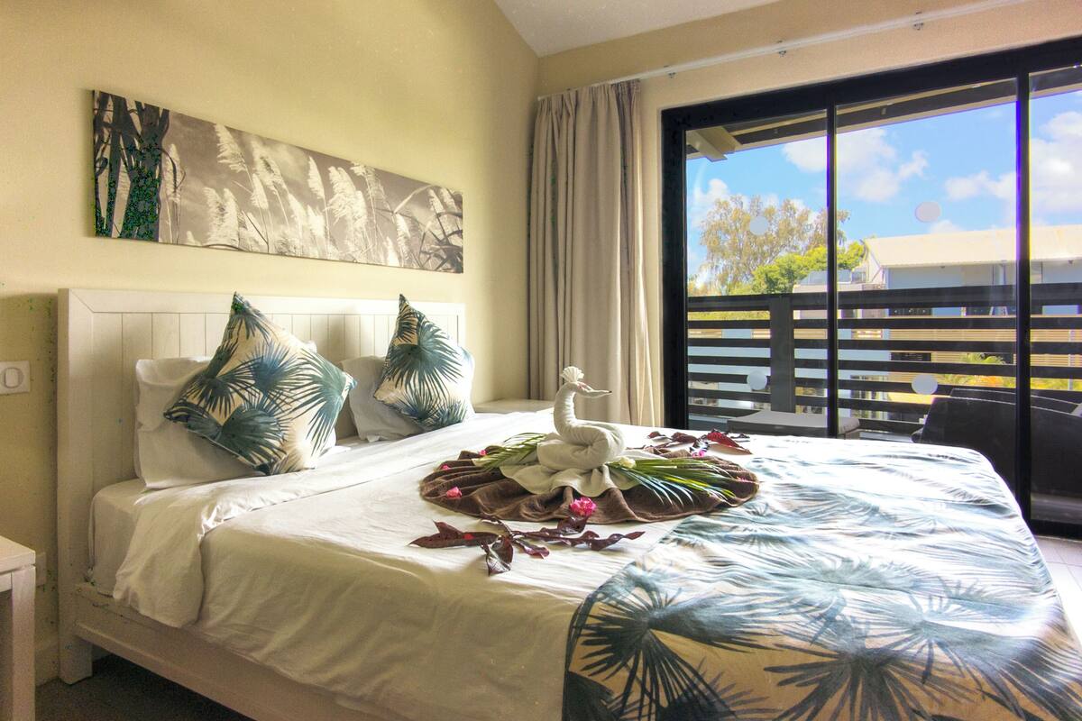 Habitación de hotel con cama, almohadas, una toalla con forma de cisne y balcón con vistas.