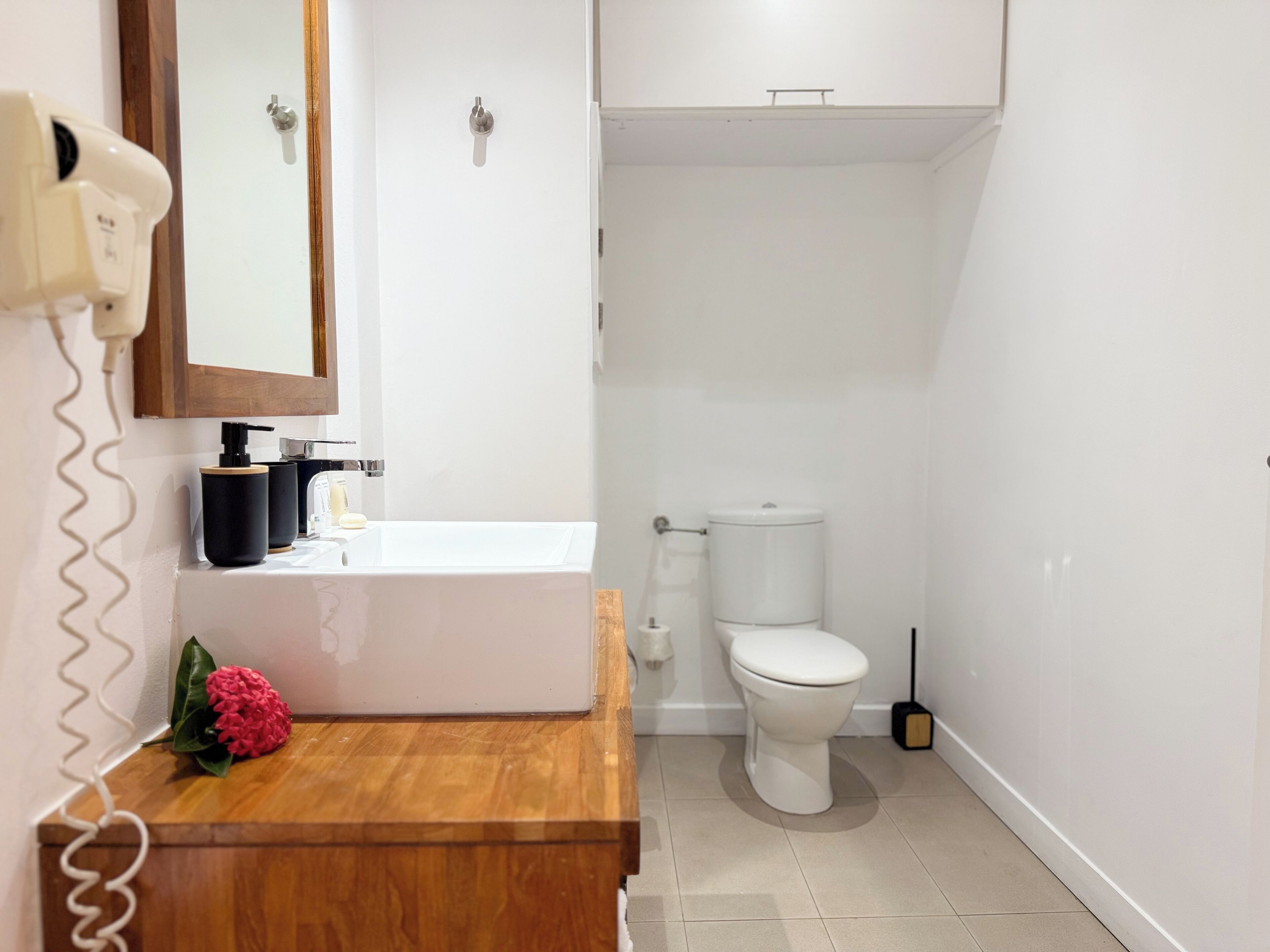 Een badkamer met een houten wastafelmeubel, een wit toilet en een spiegel boven de wastafel.