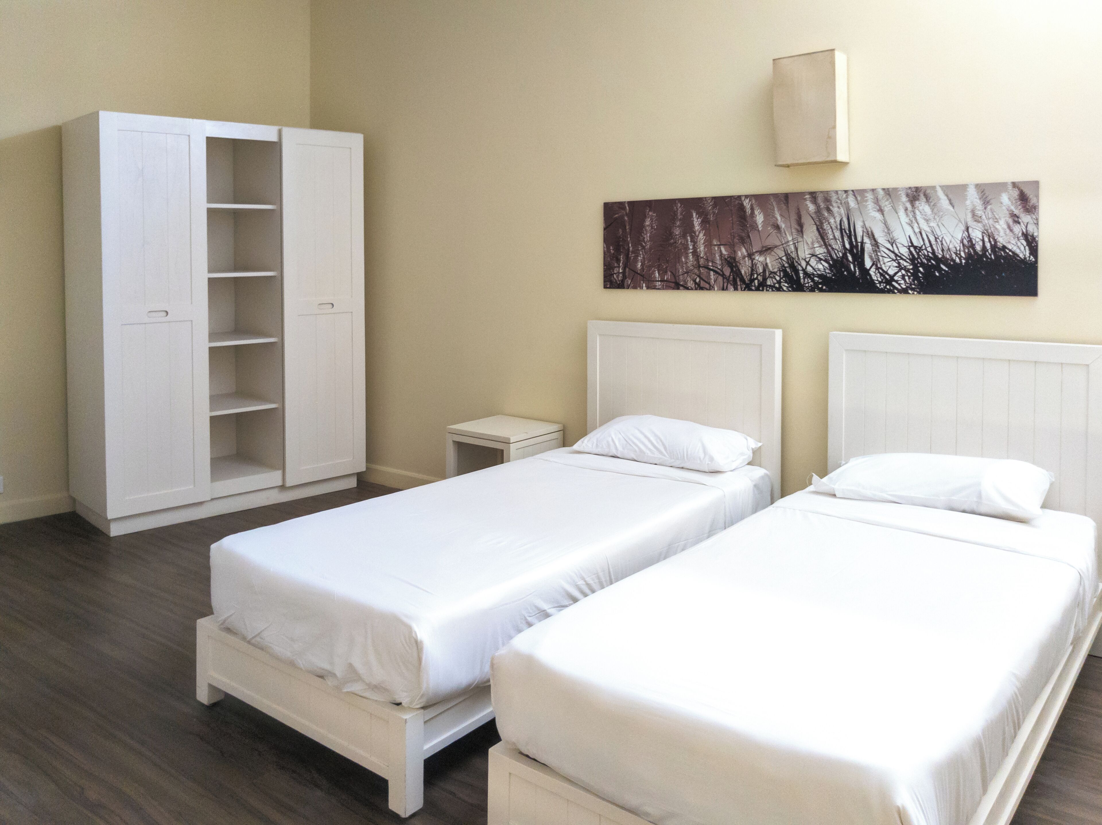 Een hotelkamer met twee eenpersoonsbedden, een kast, een klein nachtkastje en een kunstwerk aan de muur.