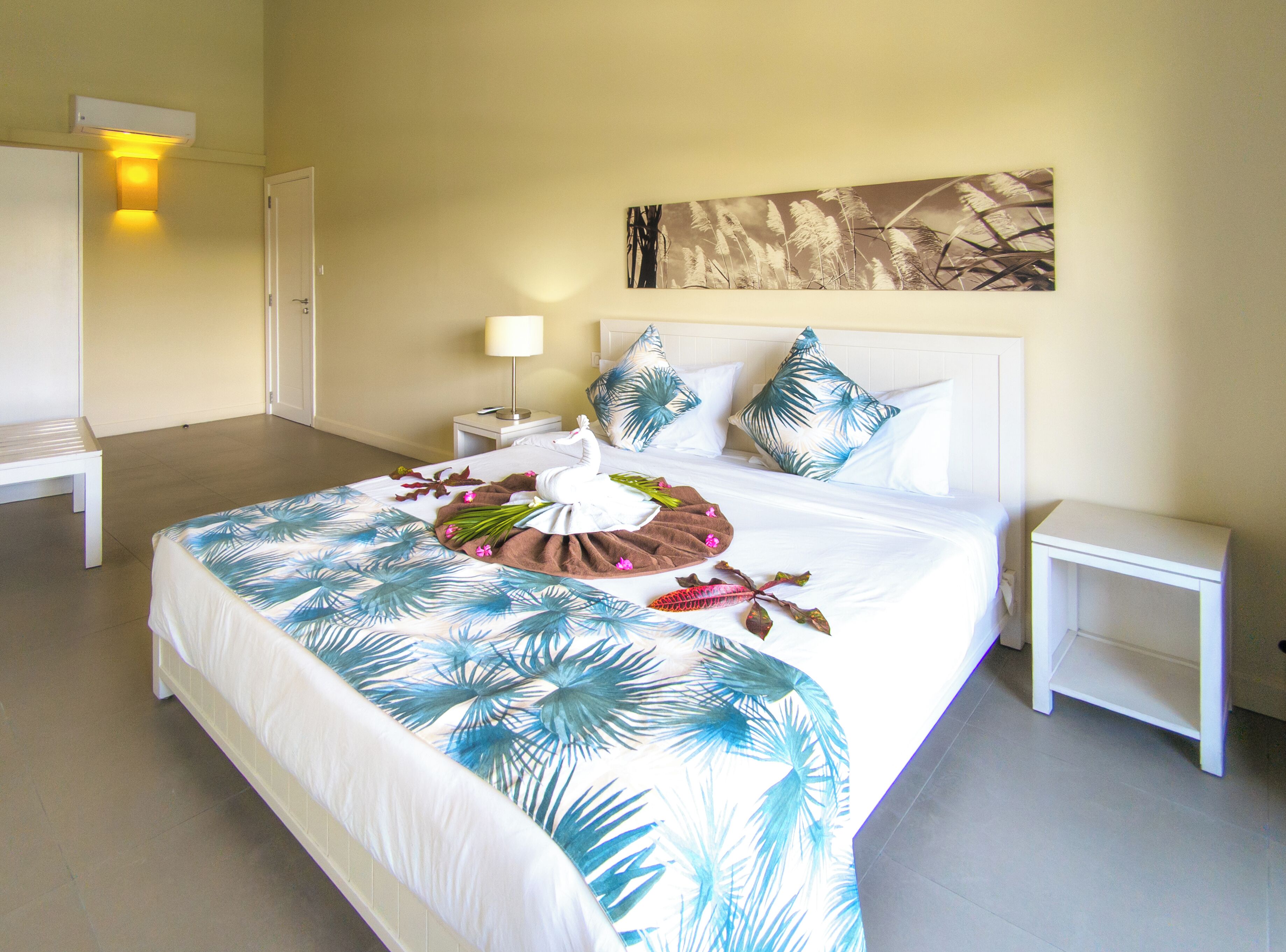 A hotel room with a large bed, white nightstands, a bench, and a wall-mounted artwork.