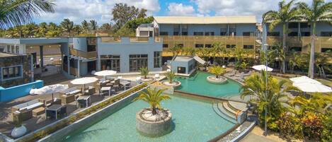 A resort with a large pool, outdoor seating, and a building with multiple floors.