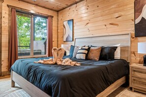 A wooden-paneled bedroom with a large bed, a nightstand, and a window with curtains. - Stellar Skies: Where the Night Sky Steals the Show (Sevierville)