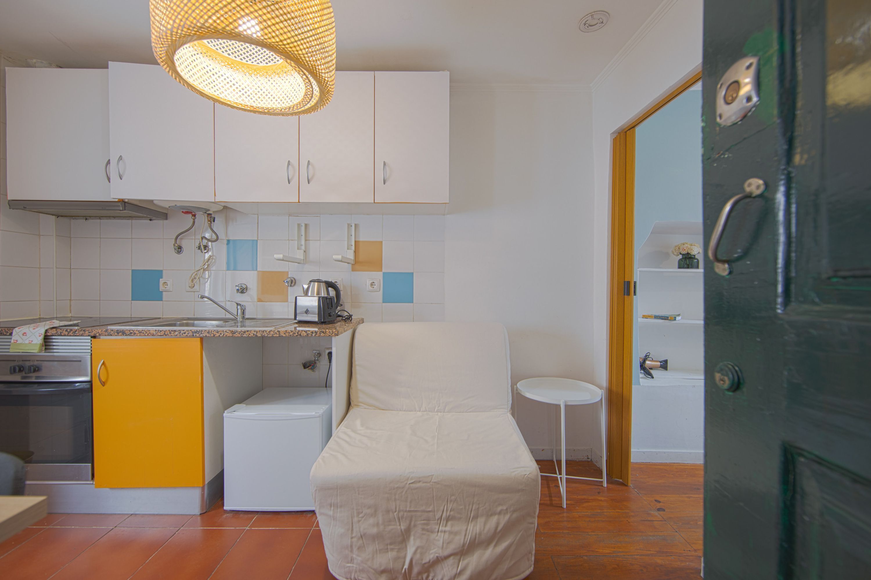 A compact kitchen with white cabinets, a yellow sink, a small refrigerator, and a white chair.