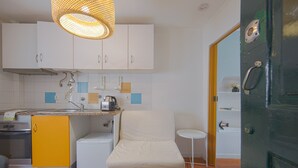 A compact kitchen with white cabinets, a yellow sink, a small refrigerator, and a white chair. - Alfama Cosy by Homing (Lisbon)