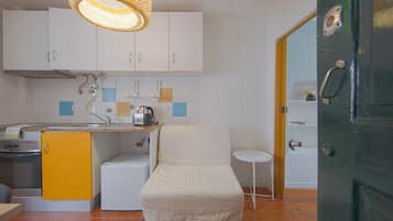 A compact kitchen with white cabinets, a yellow sink, a small refrigerator, and a white chair.