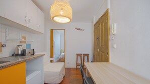 A compact kitchen with a dining area, a bed, and a bathroom visible through an open door. - Alfama Cosy by Homing (Lisbon)