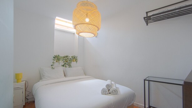 A neatly made bed with rolled towels, a bedside plant, and a hanging light fixture. - Alfama Cosy by Homing (Lisbon)