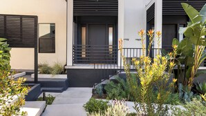 A modern building with a clean, minimalist design, featuring a flat roof, large windows, and a well-maintained garden with various plants and flowers.