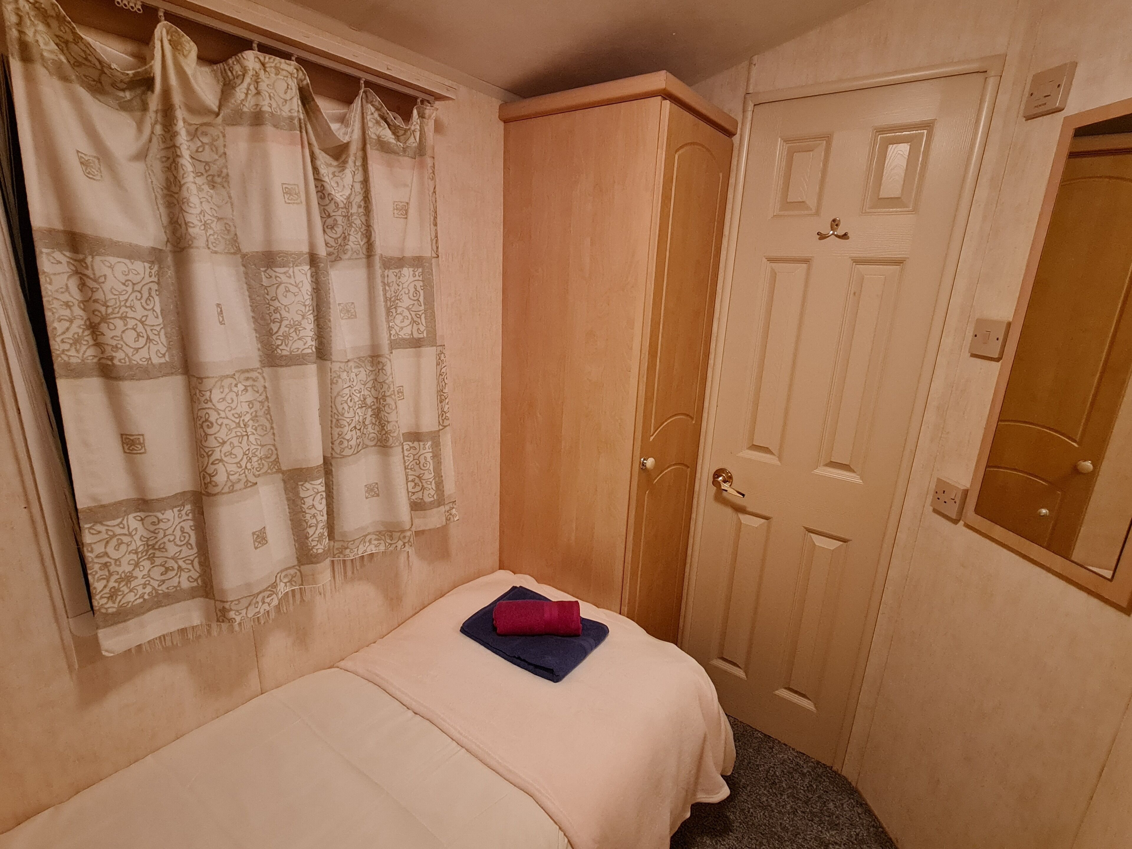 A small, cozy bedroom with a single bed, a wardrobe, and a door with a mirror.