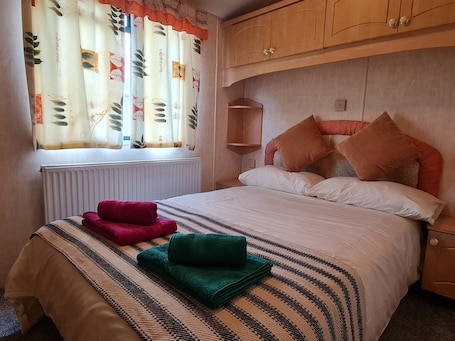 A bedroom with a bed, pillows, a radiator, a window with curtains, and a wooden wardrobe.