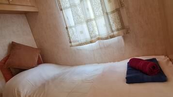 A single bed with a white duvet, a brown pillow, and a rolled blue towel.