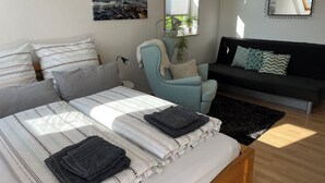 Quarto com cama, poltrona, sofá, janela com vista e um quadro na parede.