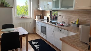 Uma cozinha moderna com armários brancos, micro-ondas embutido, pia e janela com vista para o verde.